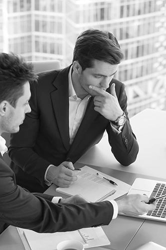 Photo en noir et blanc de deux hommes d'affaires discutant devant un ordinateur